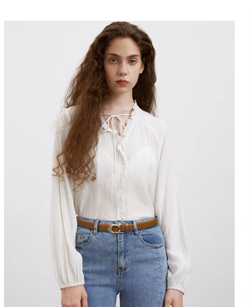 Woman wearing a white blouse with lace details and blue jeans on a plain background