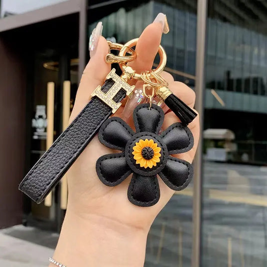 A hand holding a black leather keychain with a sunflower tassel design and gold-colored hardware.